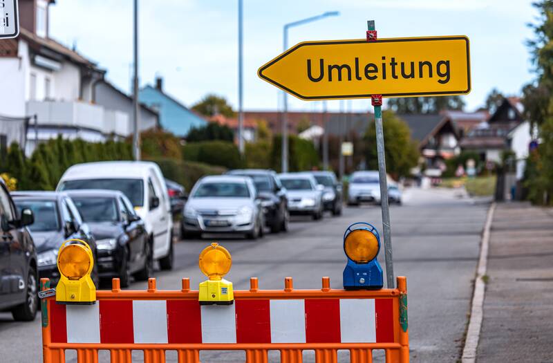 Ein gelbes Umleitungsschild, das in die linke Richtung zeigt. Unter dem Schild steht eine Baustellenabsperrung.